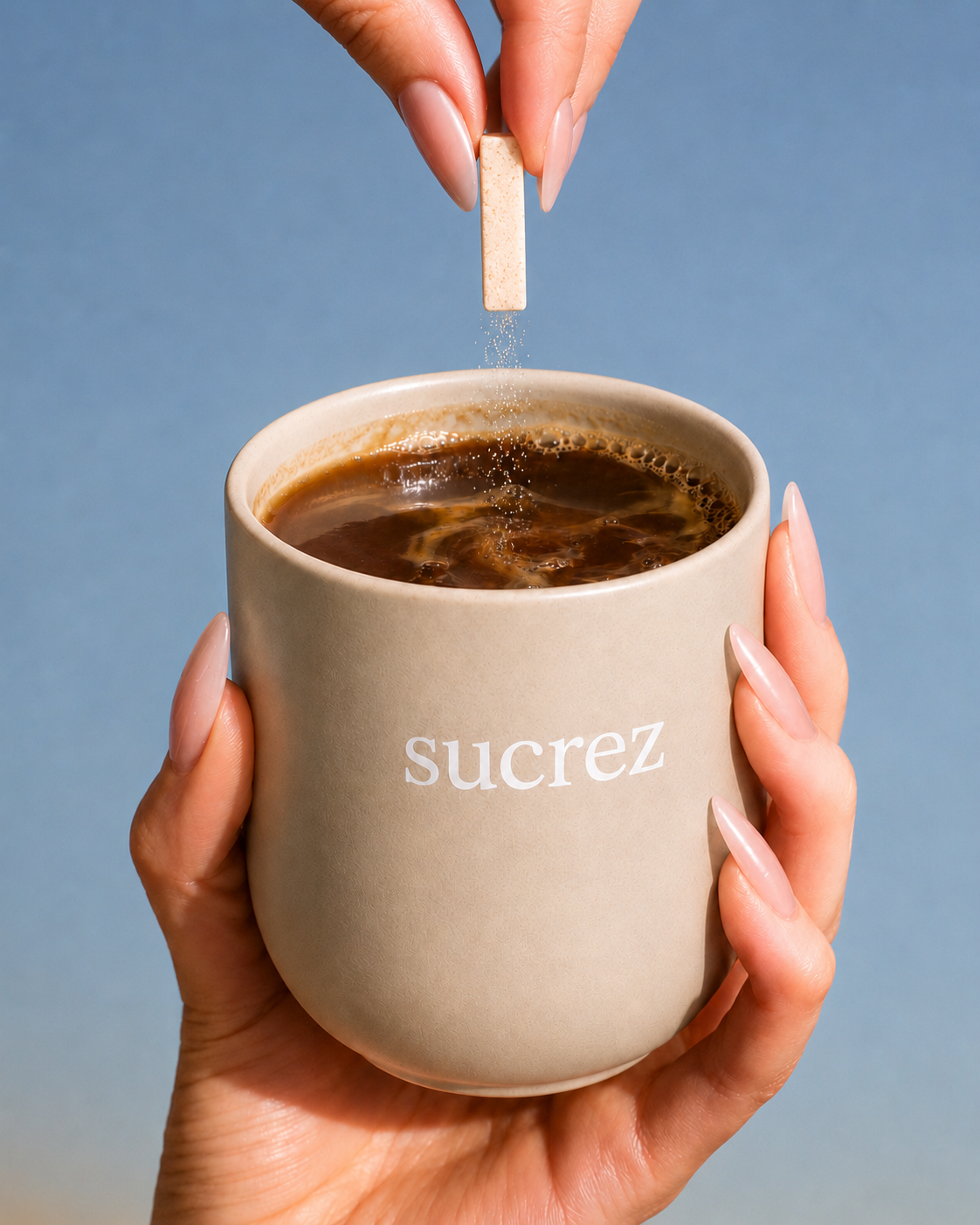 Hand holding a Sucrez mug with a sweetener tablet dropping in